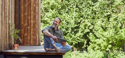 Ein Mann sitzt entspannt mit seinem Tablet auf seiner Terrasse zum Garten.