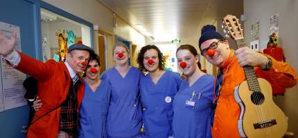 Zwei HHH Clowns stehen mit Pflegekräften, die rote Clownsnasen auf haben, in einer Einrichtung.