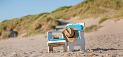 Ein Strohhut und eine Sonnenbrille liegen auf einem leeren Strandstuhl.