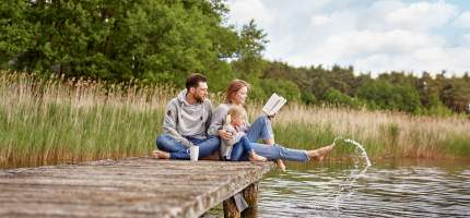 Eine junge Familie sitzt zusammen auf einem Steg am See.