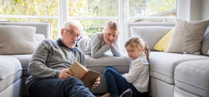 Ein Opa liest seinen Enkeltöchtern eine Geschichte vor.