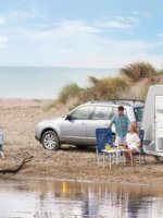 Eine junge Familie ist mit ihrem Auto und Wohnwagen an einem Strand.