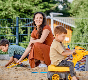 Eine Erzieherin spielt in einem Sandkasten mit zwei kleinen Kindern.