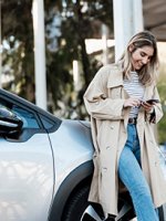 Eine junge Frau steht mit Ihrem Handy vor neuen Autos.
