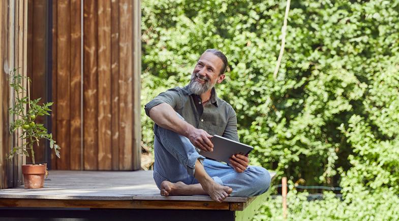 Ein Mann sitzt entspannt mit seinem Tablet auf seiner Terrasse zum Garten.