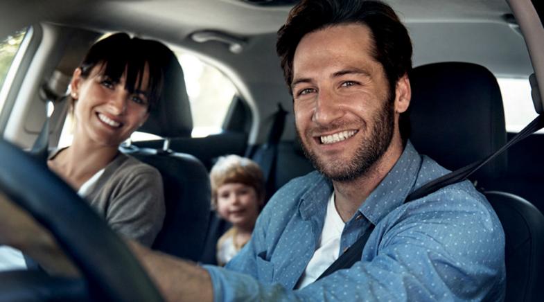 Eine junge Familie mit Kind auf dem Rücksitz im Auto.