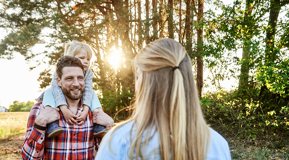 Ein junger Vater trägt seine kleine Tochter auf den Schultern.