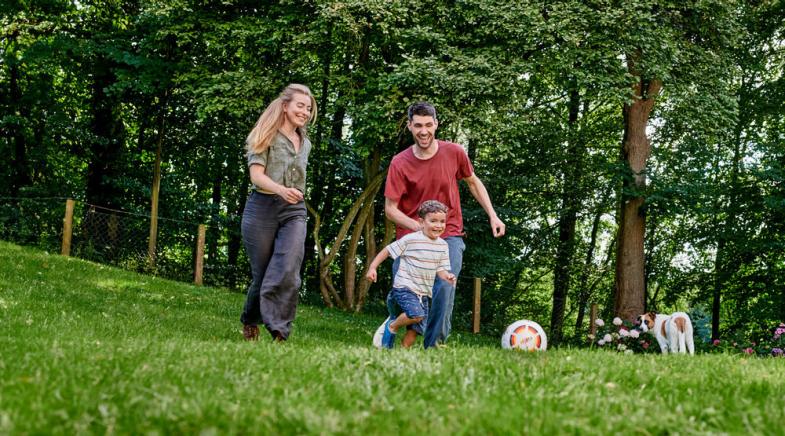 Eine junge Familie spielt im Garten Fußball.