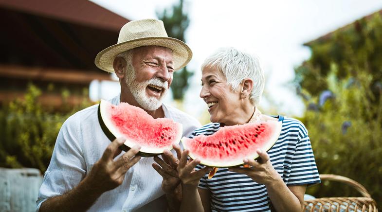 Senioren essen zusammen Wassermelone und lächeln sich an.