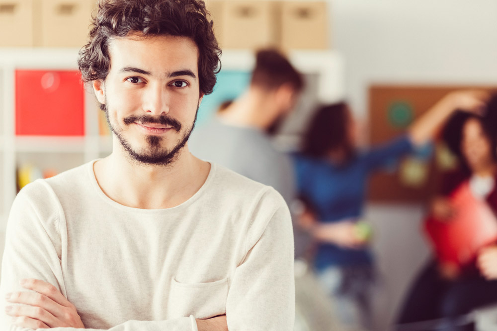 Ein Mann steht im Büro - Im Hintergrund sind Kollegen